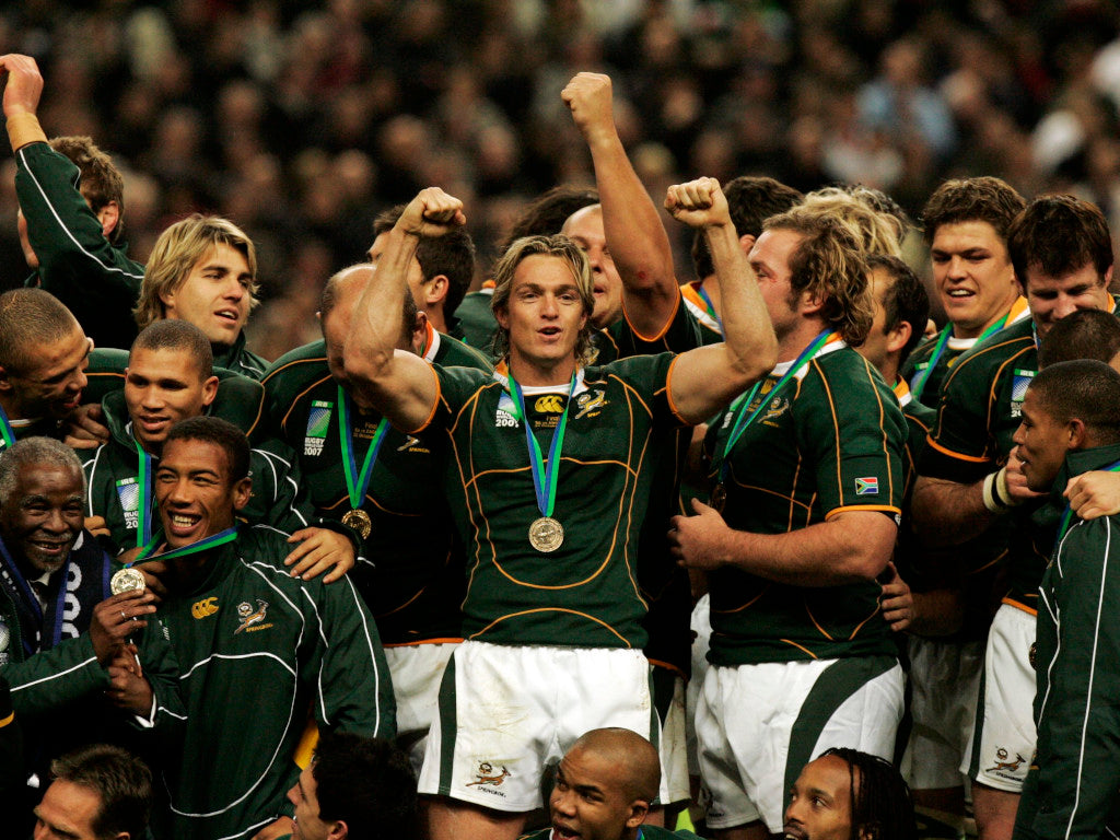Rugby players in green and white uniforms celebrating with medals on a blurred crowd background