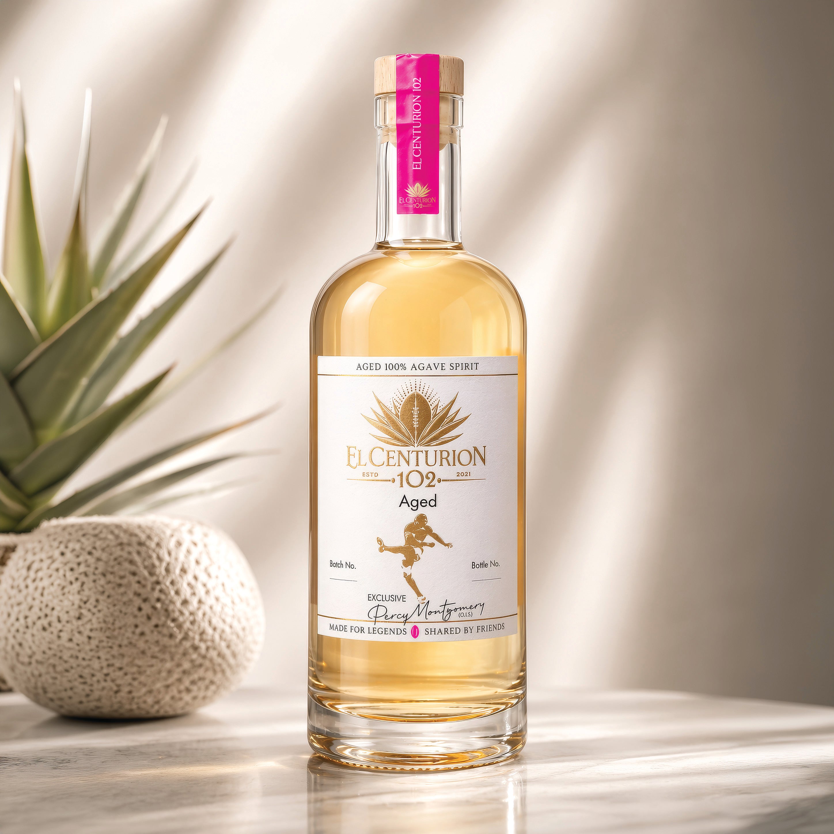 Bottle of El Centurion 102 agave spirit on a reflective surface with a plant in the background