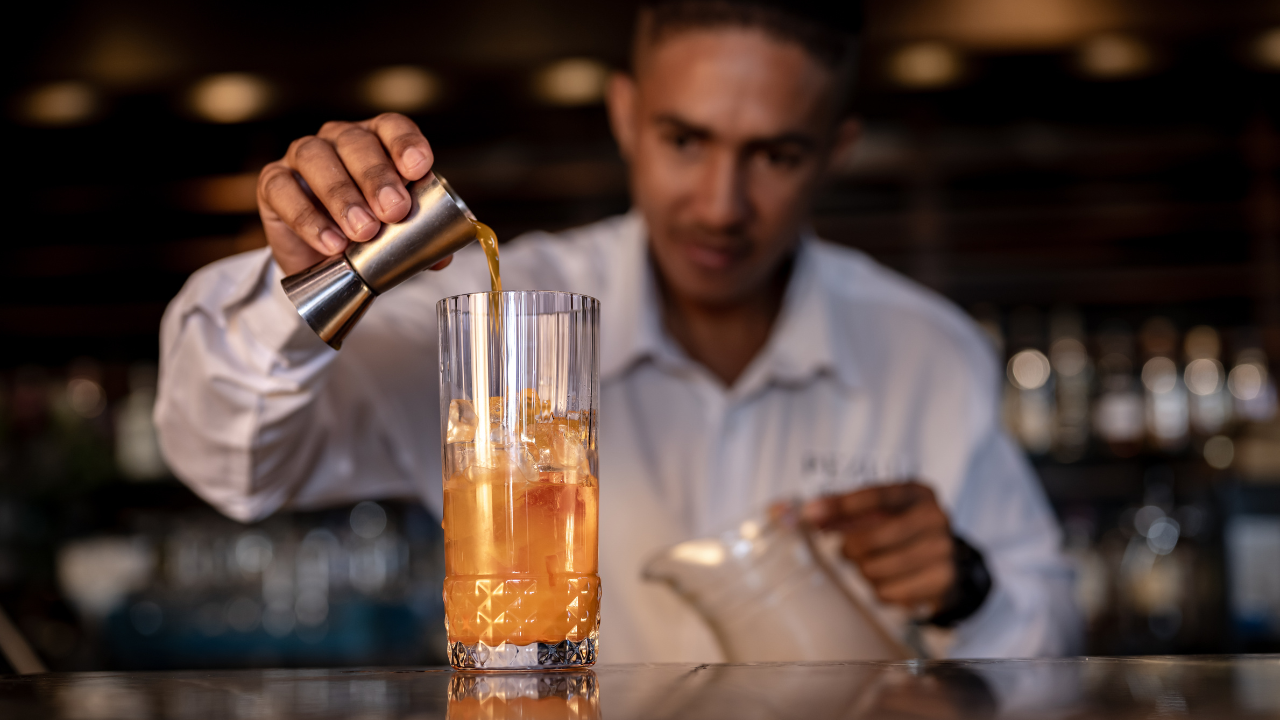 Bartender pouring a drink into a glass with a blurred bar background