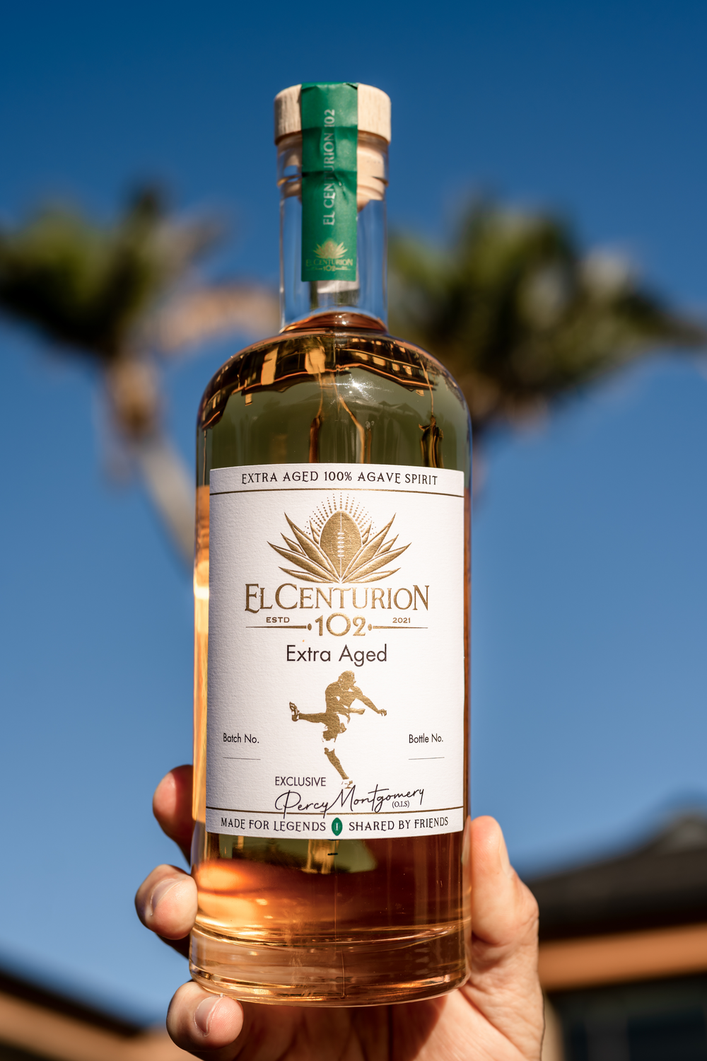 Bottle of El Centurion 102 Extra Aged held against a blurred outdoor background.