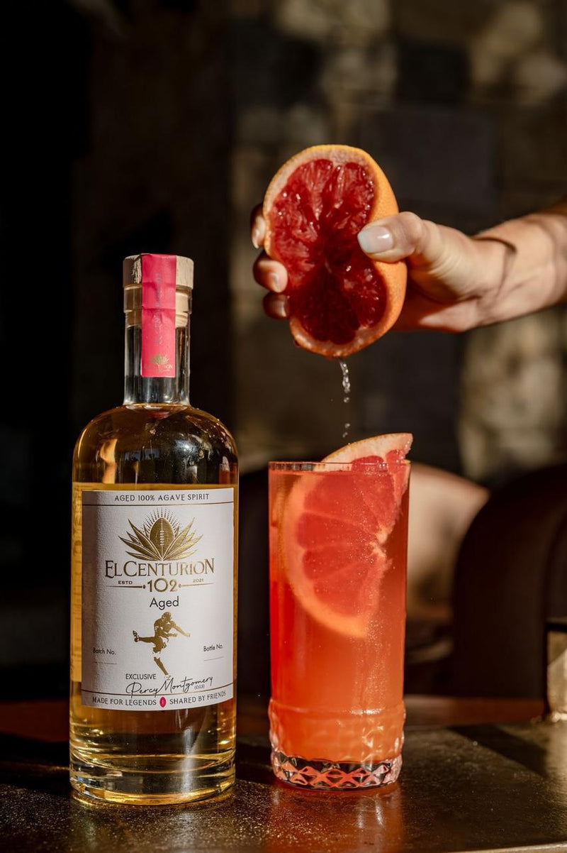 Bottle of El Centurion 102 with a cocktail and grapefruit being squeezed on a bar.